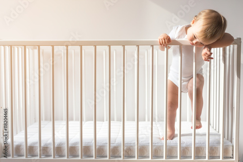 Portrait of a bored baby standing in a crib.