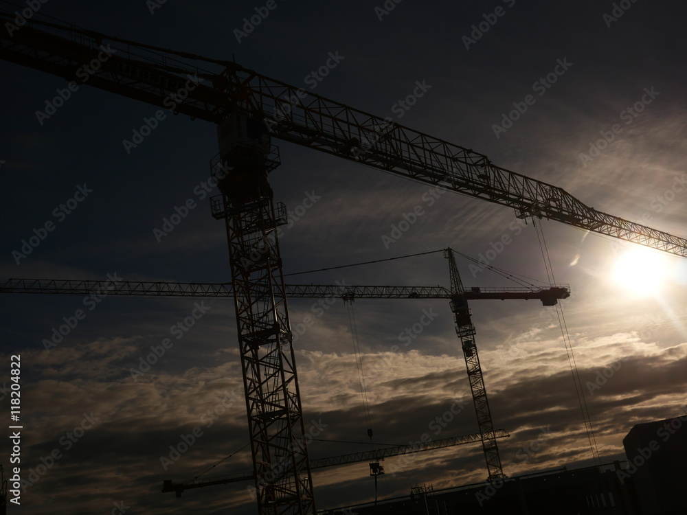 Industrial construction cranes over sun at sunrise