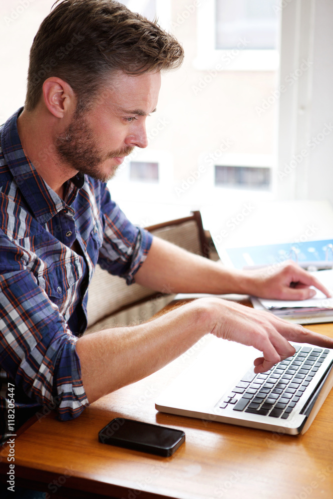 Middle age man thinking and pointing at laptop and notebook