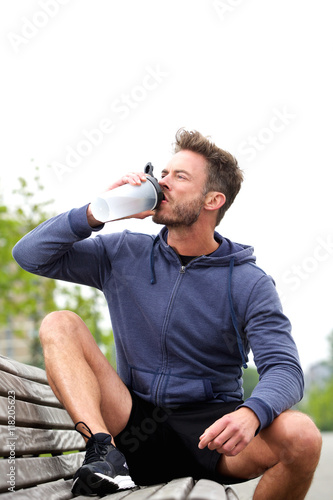 Handsome jogger sitting on bench drinking water