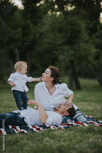Happy young family having fun, sit and lay on the grass, bowl, rising up, piggyback ride their child in park on summer sunset 