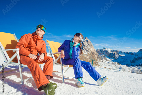 two snowboarders on top of the mountain having fun sitting on chair chaise lounge