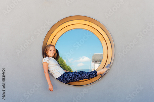 Funny little girl sitting on a round window outdoors