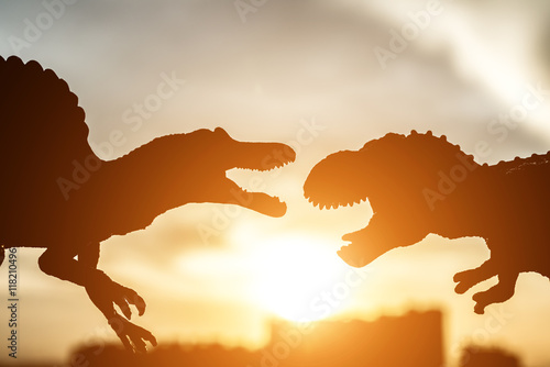 Fototapeta Naklejka Na Ścianę i Meble -  silhouette of spinosaurus and tyrannosaurus with buildings in far end in sunset time