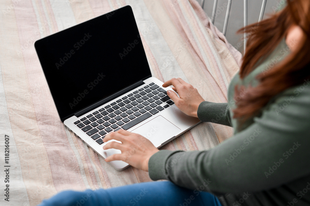 Naklejka premium Young woman using laptop on her bed