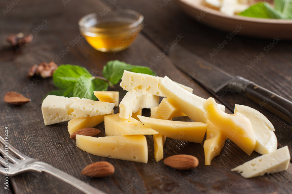 Cut cheese with fork and knife on dark wooden table, home kitchen. Cooking, food preparing, culinary concept Cut cheese with fork and knife on dark wooden table, home kitchen. Cooking, food preparing, culinary concept