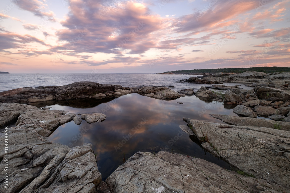 Obraz premium Landscape of a pond in shape of the star surrounded by cracked granite rocks. Standing water reflect clouds glowing by warm light of summer sunset. Russian north, Karelia, Ladoga