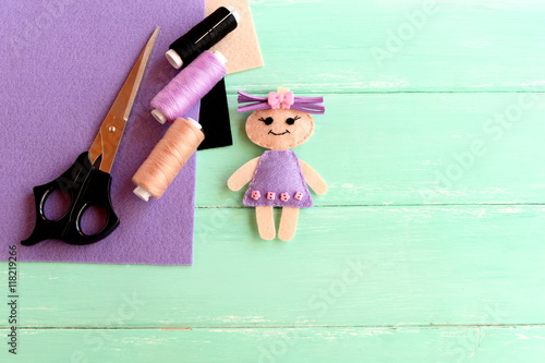 Handmade cute doll, scissors, thread, needle, felt sheets on wooden background with blank space for text. How simply and cheaply make a children toy. Creative doll crafts with felt for kids photo