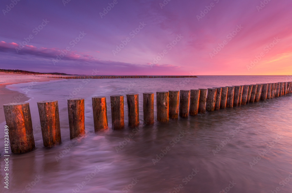 Obraz premium Colorful sunset on Batlic sea beach with wooden groyne