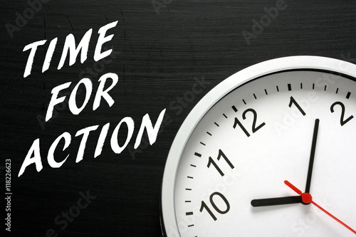 The words Time For Action written in white text on a blackboard next to a modern wall clock