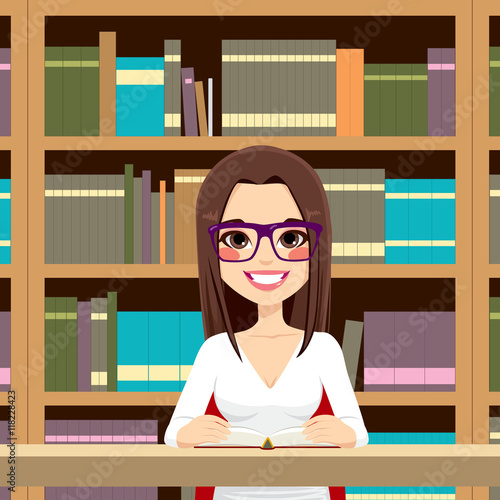 Beautiful student girl with classes happy studying in library reading a textbook