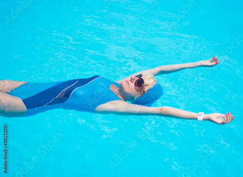 Woman is relaxing in a pool in the blue swimsuit and sunglasses.