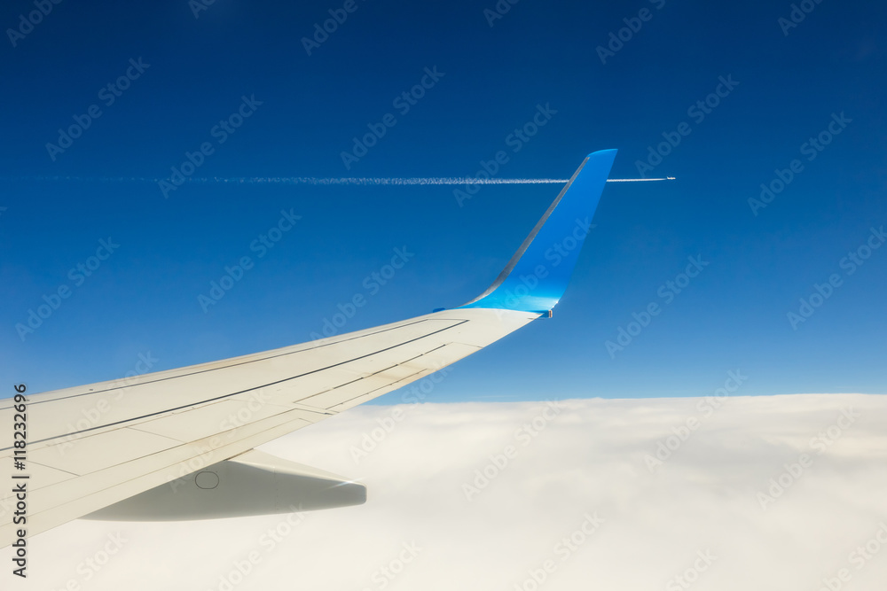 Wing of an airplane flying above the clouds on blue sky background Wing of an airplane flying above the clouds on blue sky background