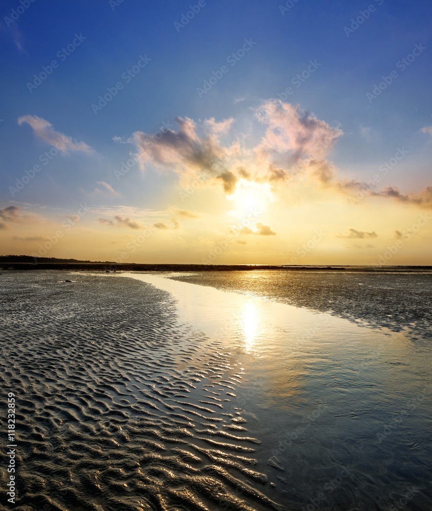 Colourful sunrise and the sand during low tide ocean water