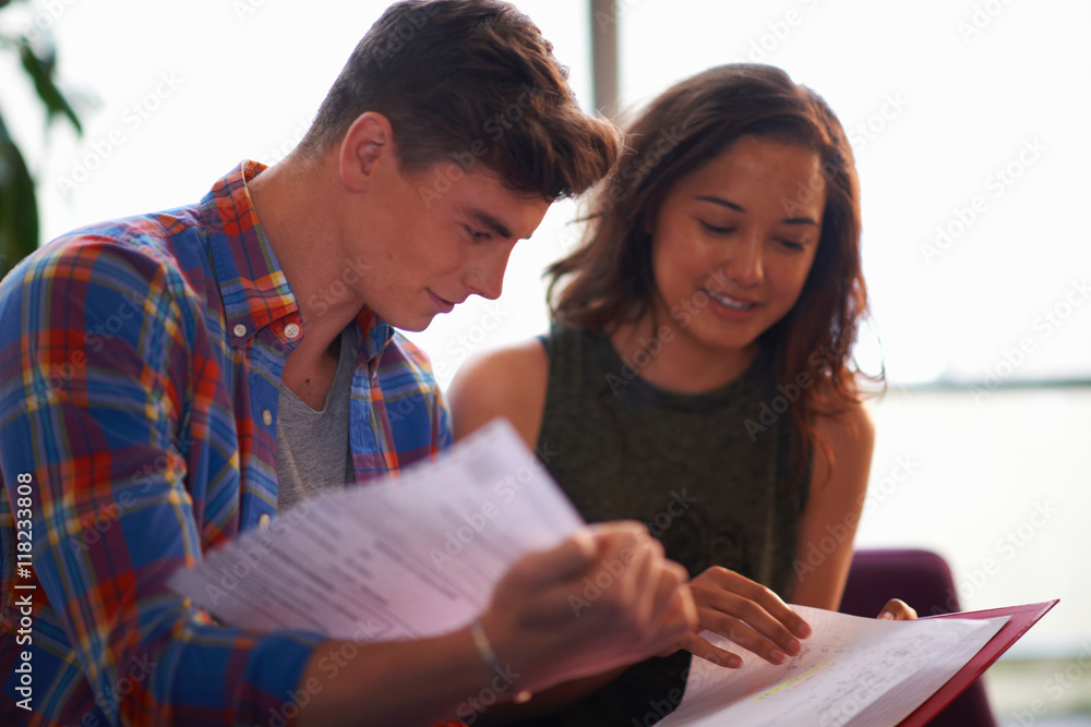 Young female and male college students reading file in common room Young female and male college students reading file in common room