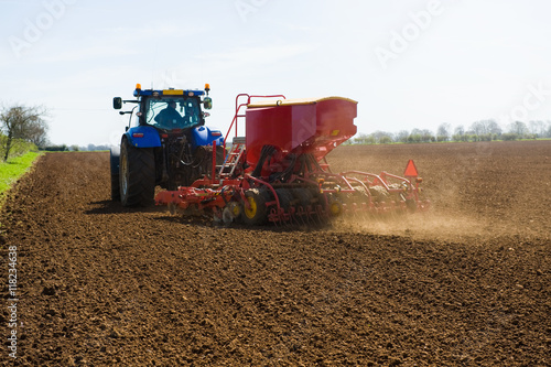Farm tractor and seed drill sowing ploughed field in spring