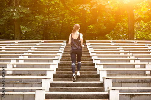 Rear view of young woman training, running up stadium stairway photo