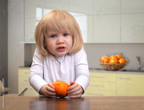 Very sad little girl with mandarin in the kitchen.