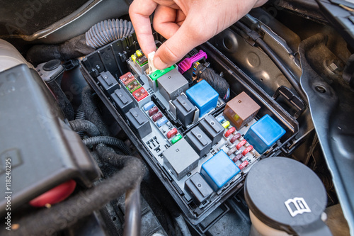 Hand checking a fuse in the fuse box of a modern car engine