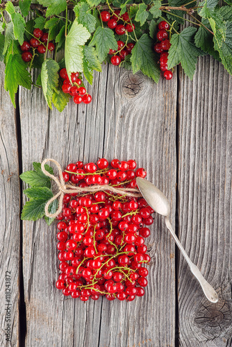 red currants like vial with twine and metal spoon on wooden background, creative idea for healthy lifestyle, raw food