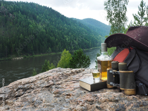 Bottle with alcohol and tourist equipment on the background of forest