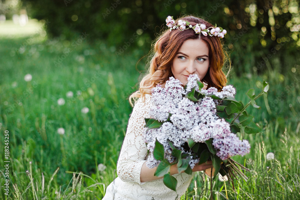 Fototapeta premium Spring beauty girl with long red hair in a white plate outdoors. Flowering tree. Romantic portrait of young woman with bouquet.