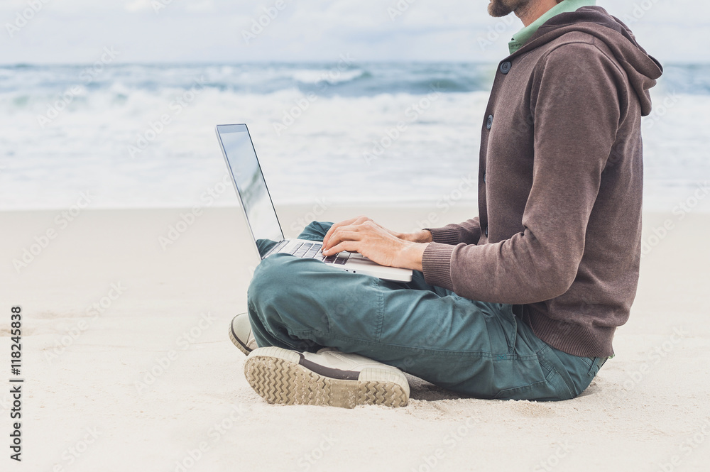 Young man working on laptop while sitting on the beach, freelance working, social networks concept