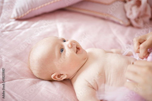 Little blue-eyed girl laugh while lying on pink blanket