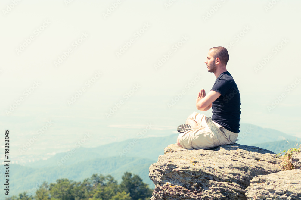 Young man meditating on top of the mountain