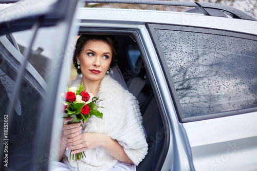 Beautiful bride sits in white car holding her bouquet of roses