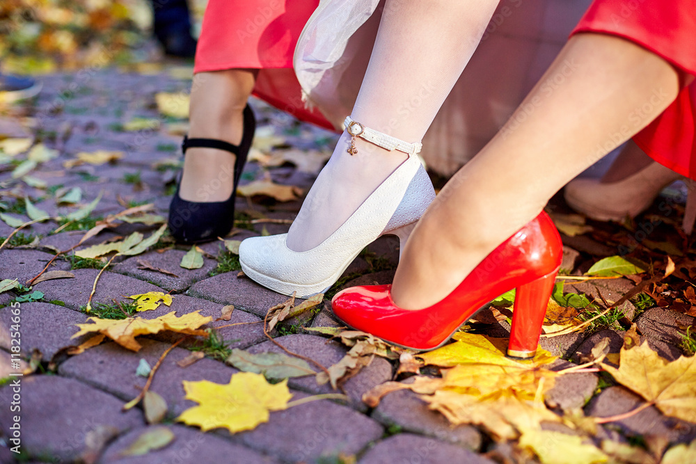 Bride's leg in white shoe and bridesmaids' feet in red and black