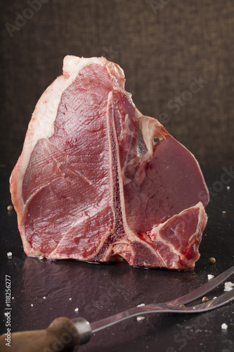 Red Raw fresh T-bone steak cut put with salt and pepper seasoning on black background