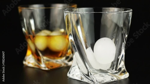 Whiskey being poured into a glass with ice against a black background