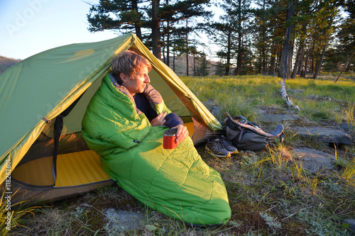 Male camper sitting up in sleeping bag watching sunset on Midnight Ridge, Colville National Forest, Washington State, USA photo
