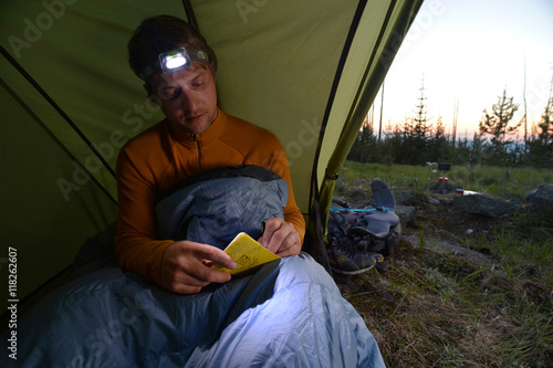 Male camper in sleeping bag writing his journal at dusk on Midnight Ridge, Colville National Forest, Washington State, USA photo