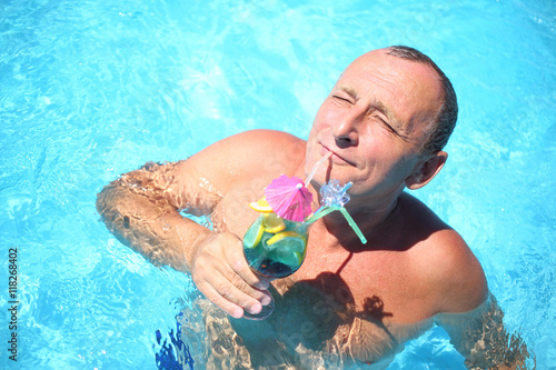 Portrait of a happy senior with a tropical cocktail at the swimming pool