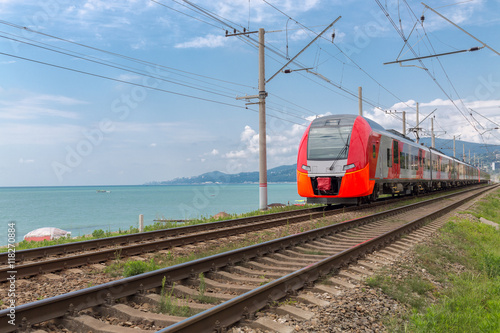red train rides on rails along the seashore
