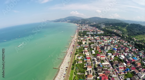 Beach and many houses in coastal city near mountains at summer sunny day. Aerial view. Photo with noise from action camera.