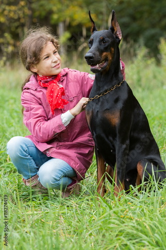 Little curly girl with red scarf is holding the dog and hugging it, focus on a dog. © Pavel Losevsky