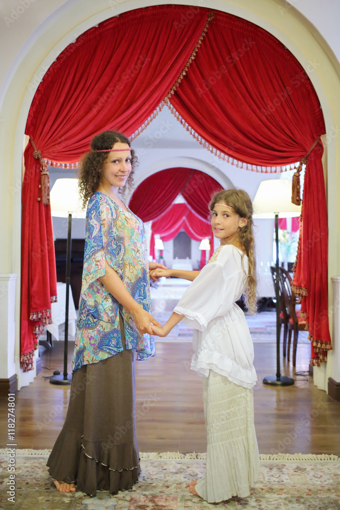 Fototapeta premium Mother and daughter (with model release) in ethnic dress holding hands in a room in medieval style of the Hotel Bogatyr