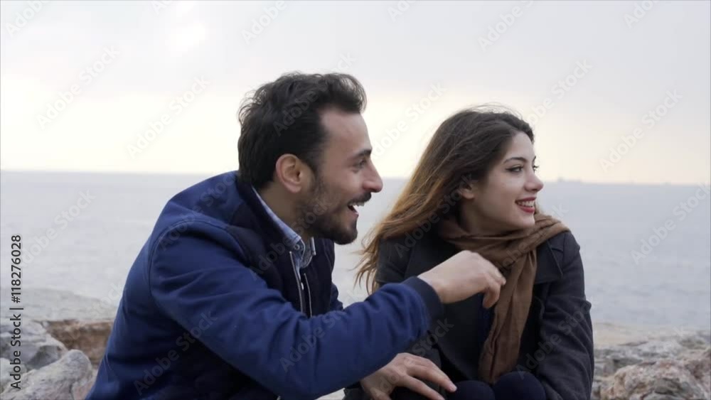Young couple sitting next to the sea on the stone Young couple sitting next to the sea on the stone