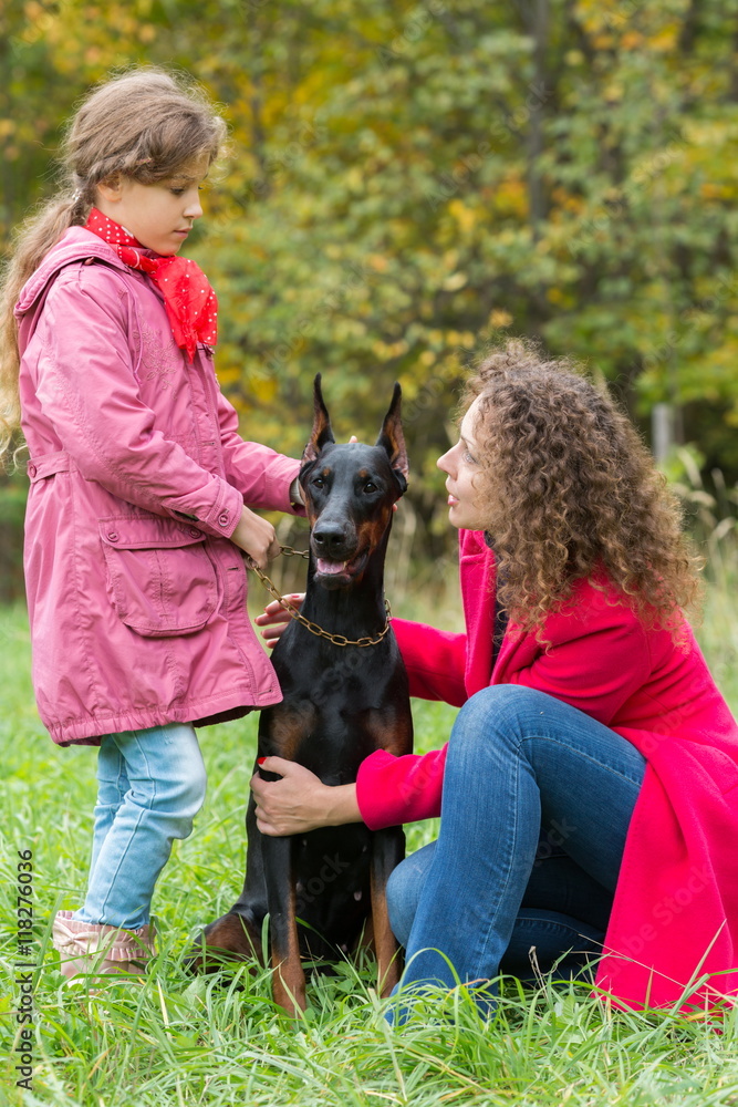 Little curly girl is holding the dog and her mother is hugging it in park. Little curly girl is holding the dog and her mother is hugging it in park.