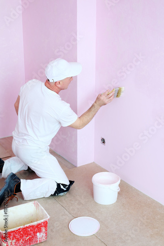 Man in white clothes covers the walls pink decorative plaster photo