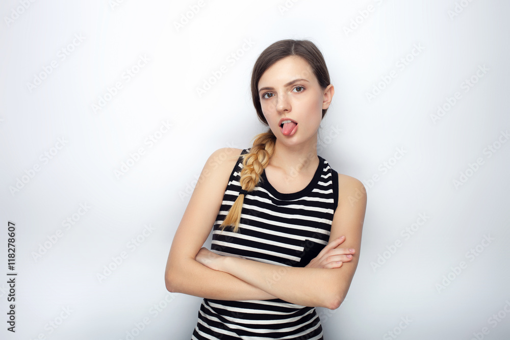 Portrait of naughty young beautiful woman in striped shirt crossed hands showing tongue posing for model tests against studio background Portrait of naughty young beautiful woman in striped shirt crossed hands showing tongue posing for model tests against studio background