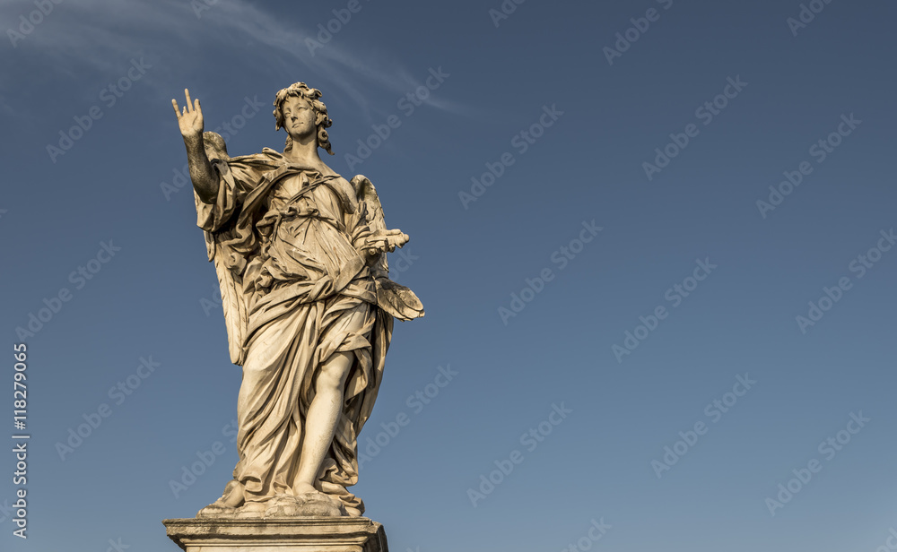 A large, stone statue of an angel, against a deep blue summer sky