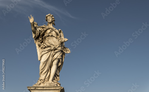 A large, stone statue of an angel, against a deep blue summer sky