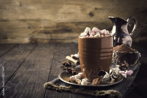 Cup of hot chocolate with mini marshmallows and winter spices on dark wooden background with copy space.