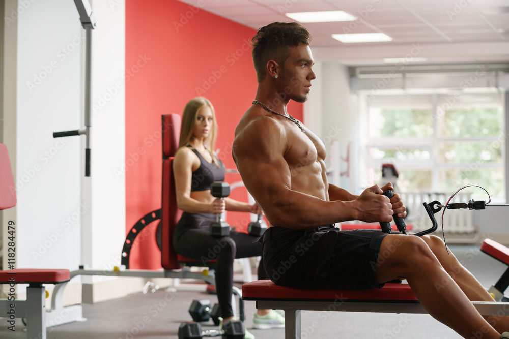 Sexy guy trains on simulator and girl looks at him Sexy guy trains on simulator and girl looks at him