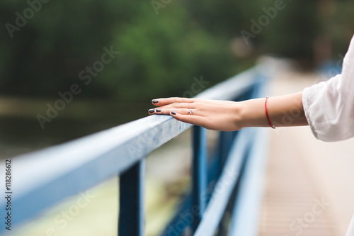 Sophisticated girl's hand touches the railing of the bridge on the background of the river