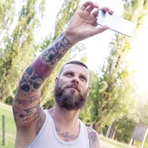 tattooed bearded man takes a selfie in the park